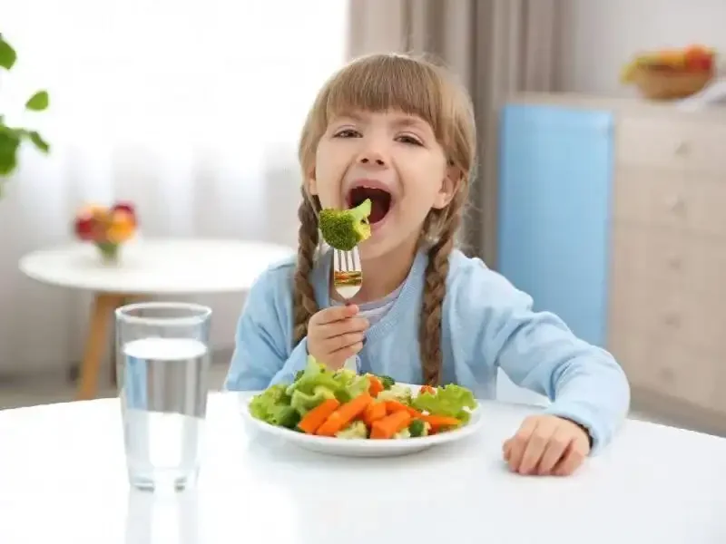 کودکی در حال خوردن انواعی از سبزیجات